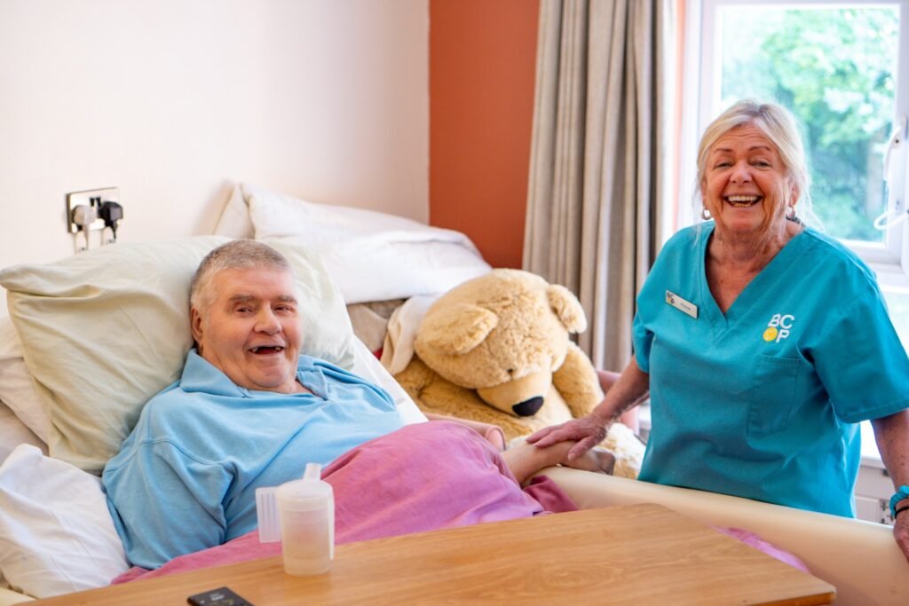 an older person in bed with a care assistant next to them