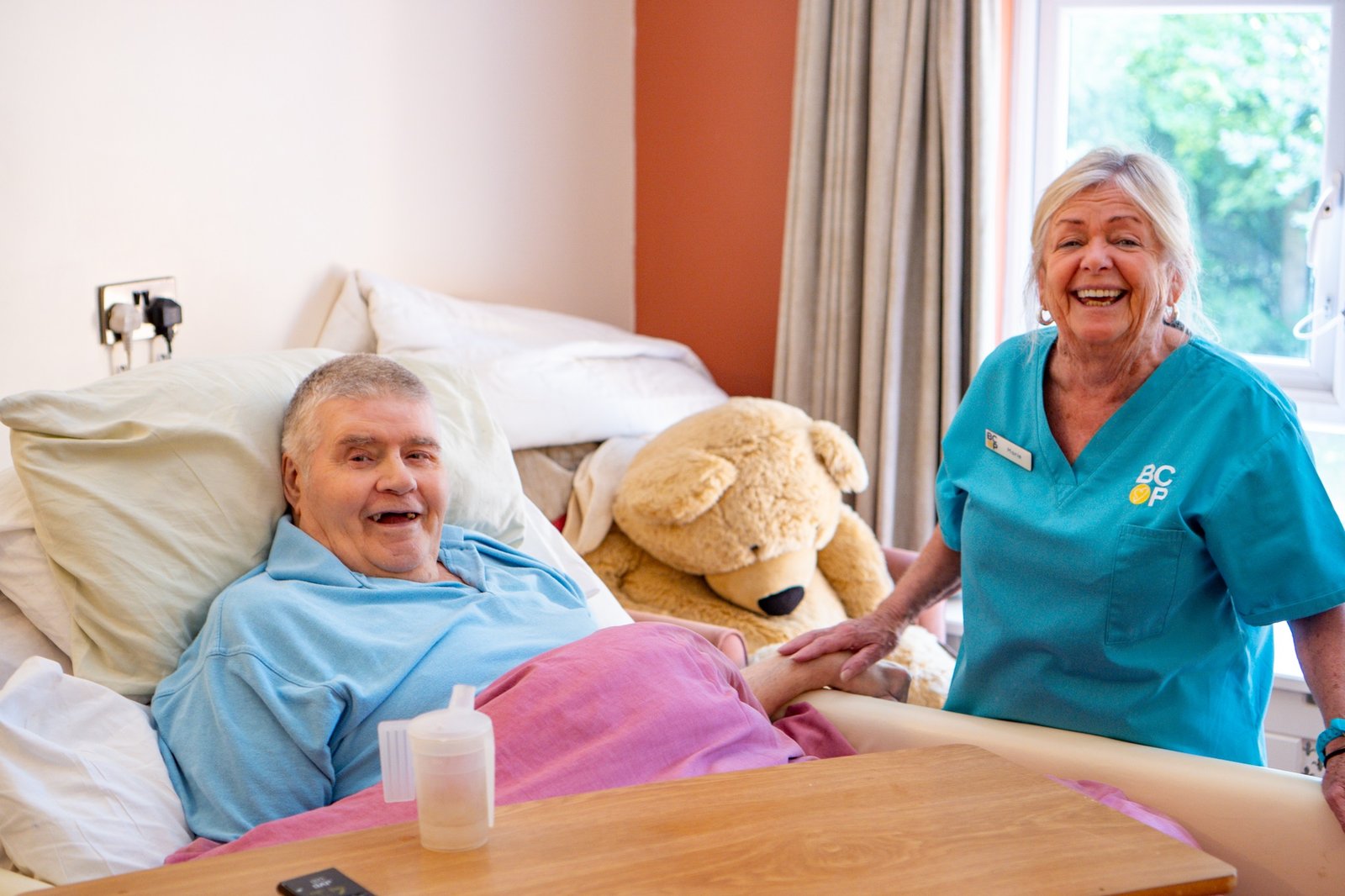 an older person in bed with a care assistant next to them